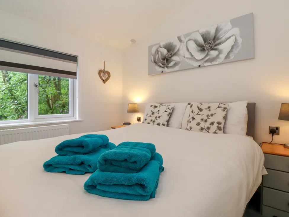 A bedroom with a white bed and folded teal towels beside a window.
