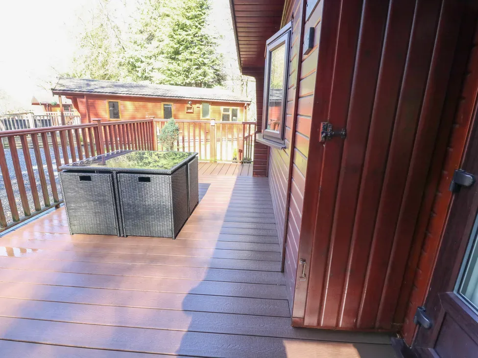 A wooden outdoor deck with a railing and a rectangular planter beside a cabin.