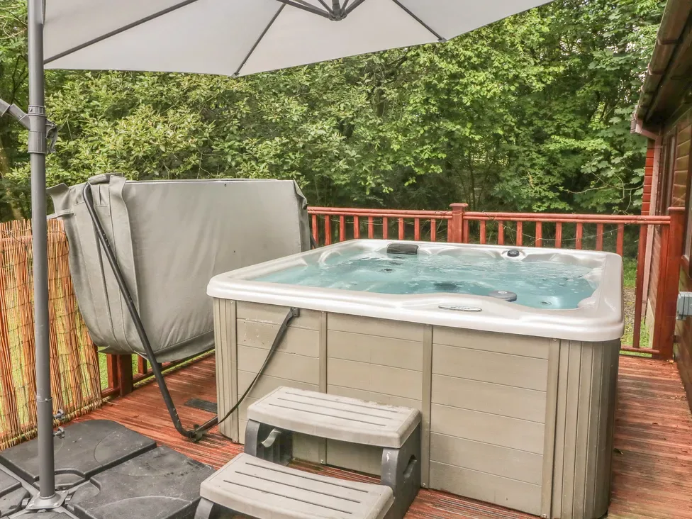 A hot tub sits on a wooden deck beneath a patio umbrella, with trees beyond the railing.