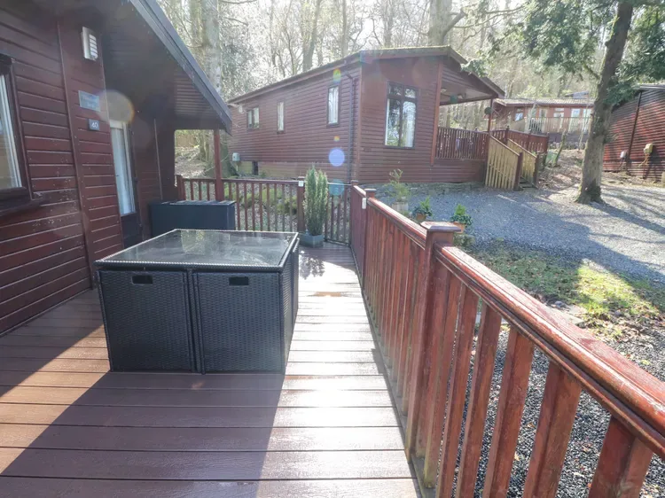 A wooden deck with dark outdoor seating overlooks a wooded cabin area.
