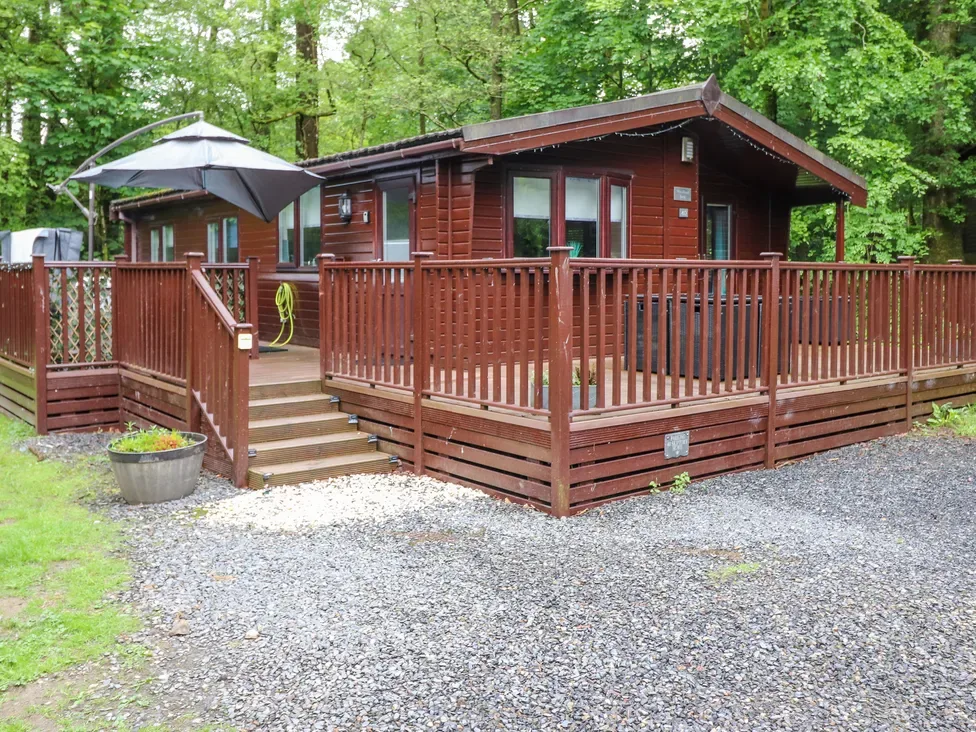 A wooden cabin with a raised deck and steps stands among leafy trees.