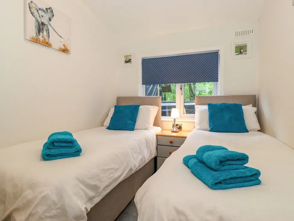 A bedroom with two beds, teal towels and pillows, and a window with a blue blind.