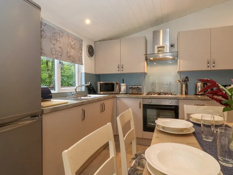 A kitchen with pale cabinets, a cooking range, and a dining table set with dishes.