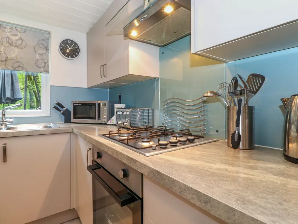 A kitchen with a gas cooktop, oven, microwave, sink, and utensils on the counter.