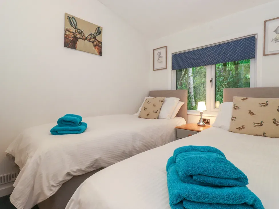 A twin bedroom with white bedding, blue towels, and animal-print cushions.