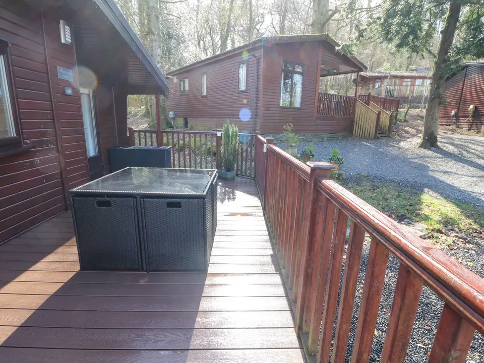 A wooden deck with a glass-top table overlooks a gravel courtyard and wooden cabins.