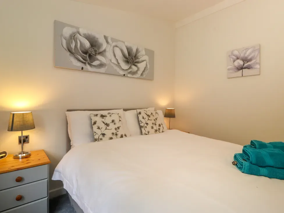 A bedroom with a bed, floral pillows, bedside tables, lamps, and folded towels.