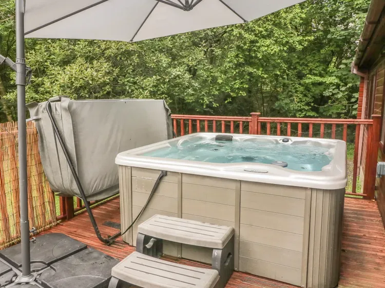 An outdoor hot tub sits on a wooden deck beside a patio umbrella.