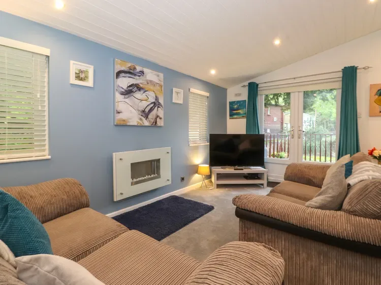 A living room with seating, a television, and large windows opening onto a balcony.