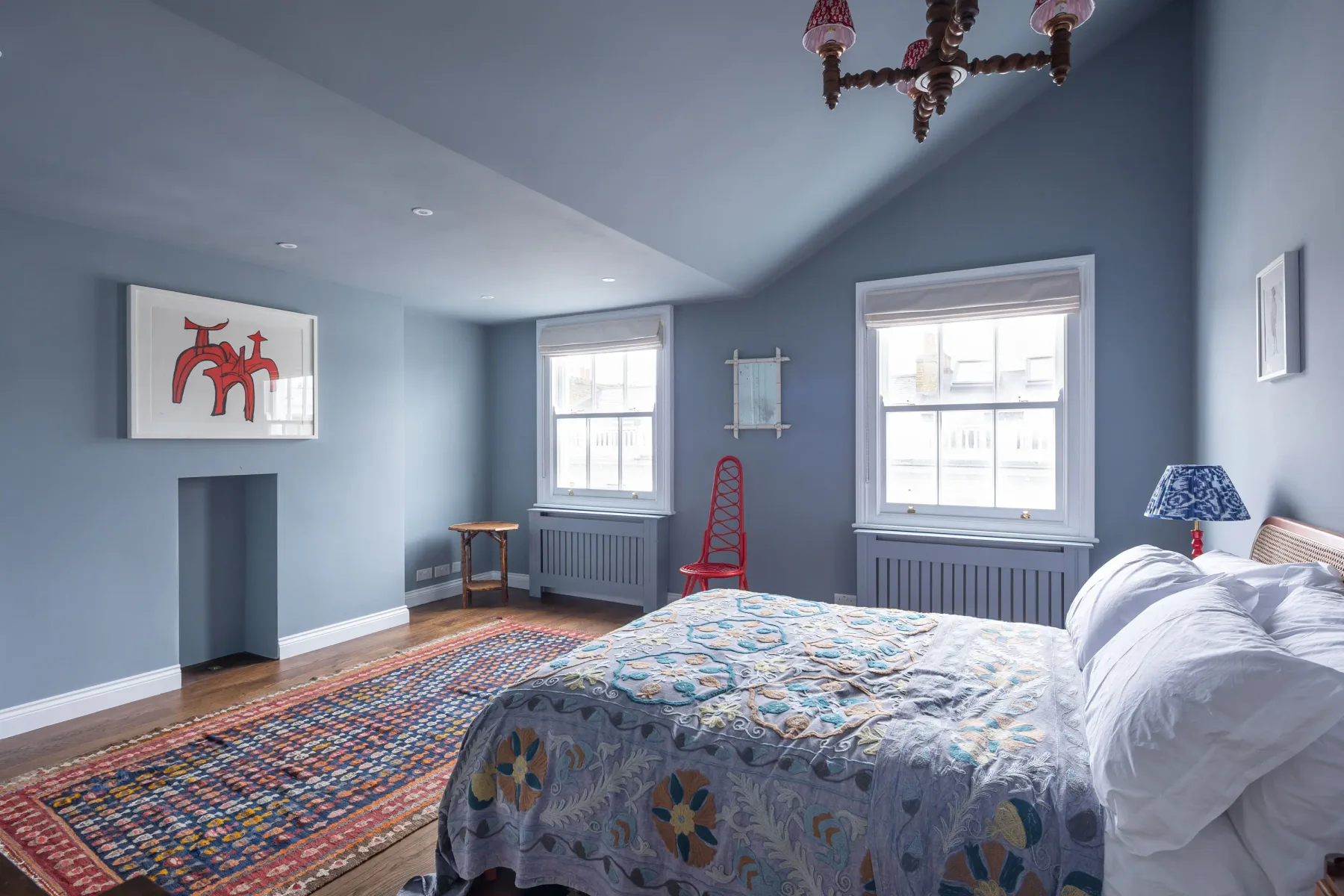 A bedroom with a large bed, colorful rug, and two windows.
