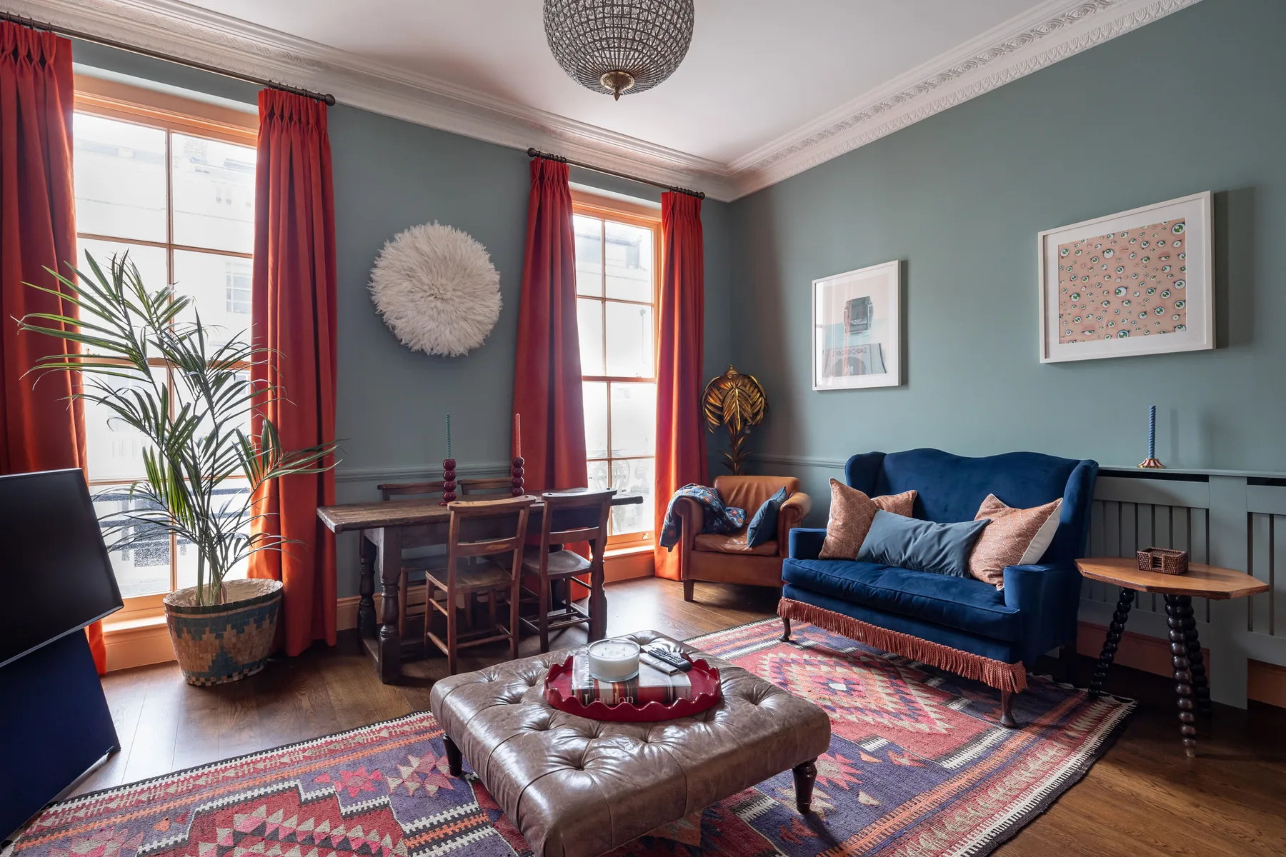 A sitting room with blue seating, a patterned rug, and tall curtained windows.