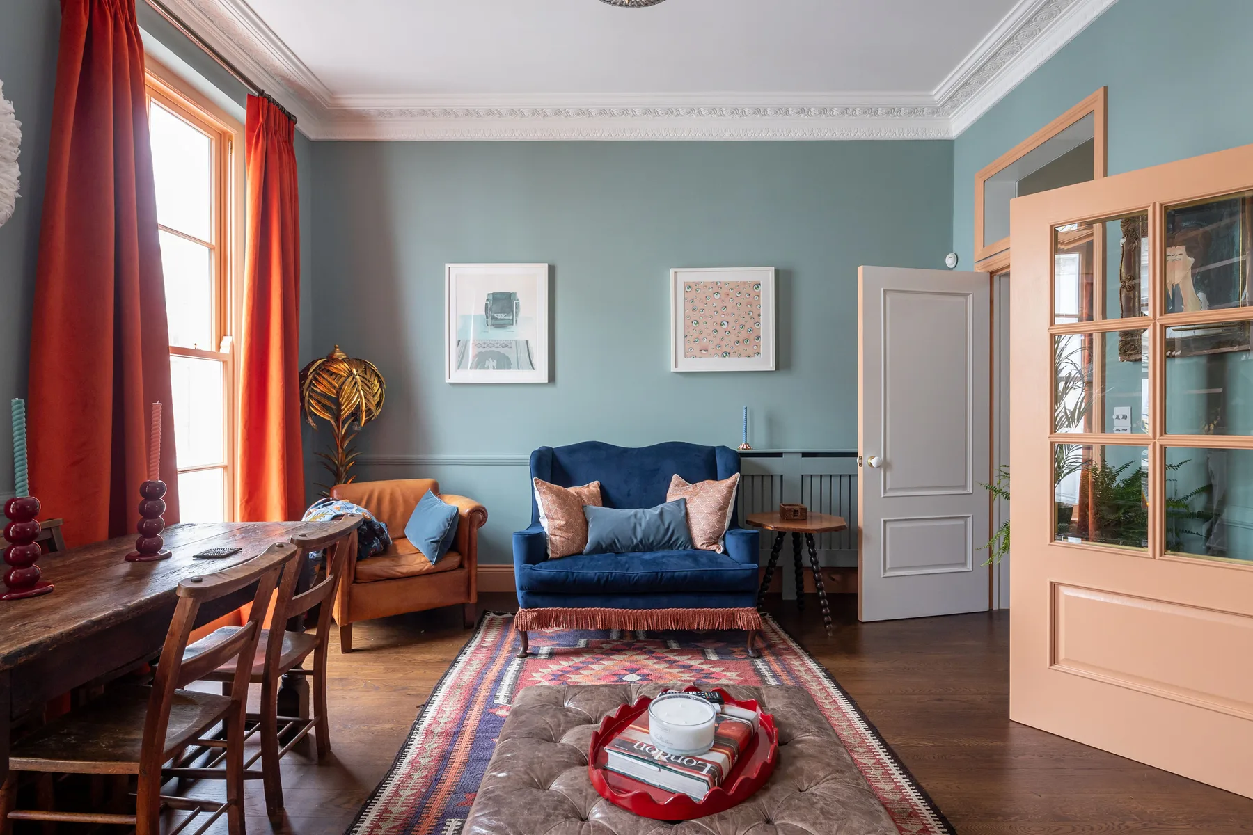 A sitting room with blue seating, framed artwork, and tall windows.