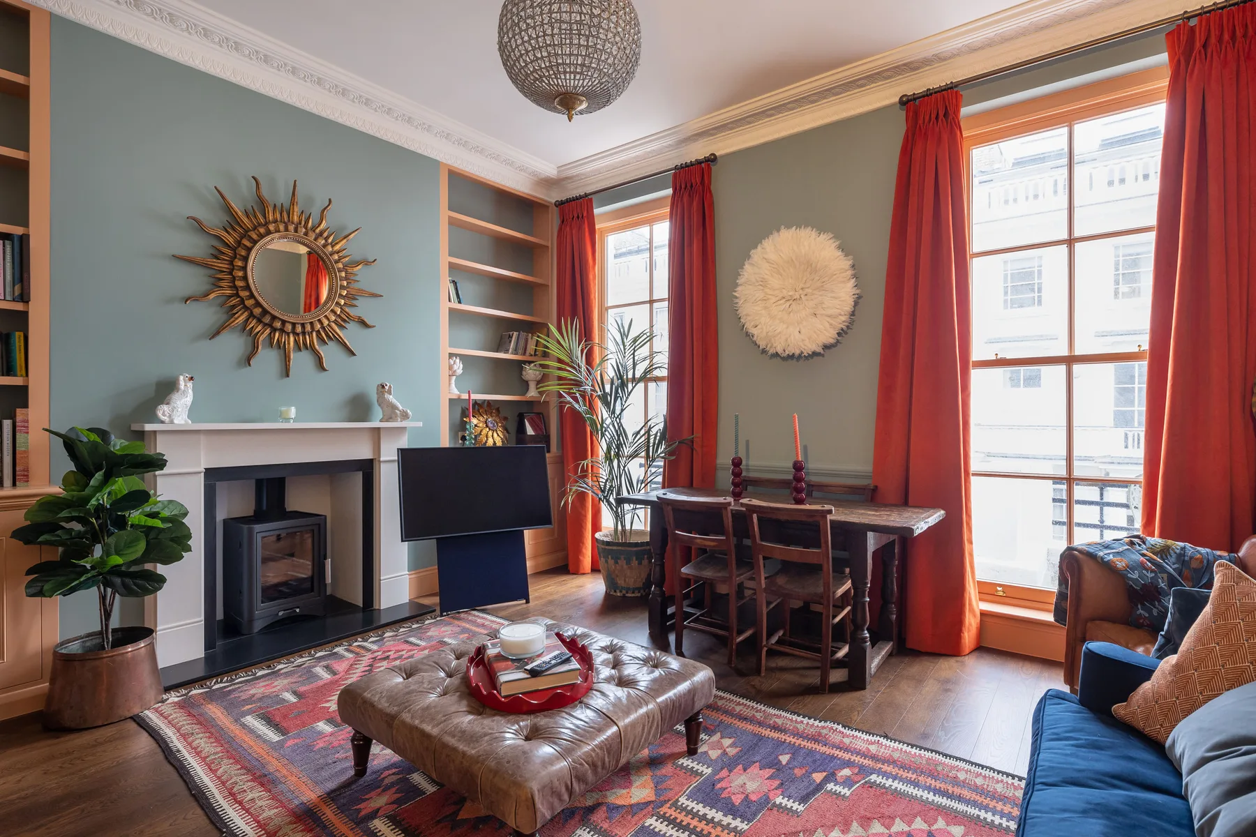 A living room with a fireplace, seating, and tall windows framed by red curtains.