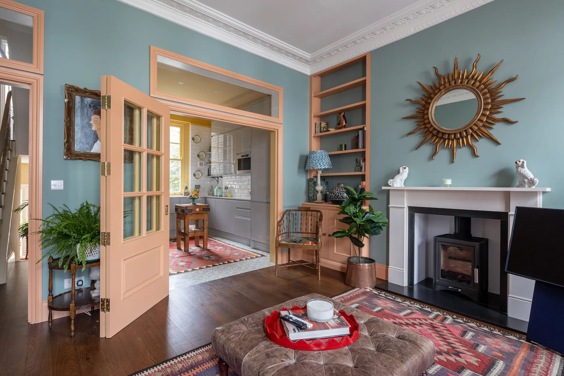 A living room with a fireplace, sunburst mirror, and an open doorway to the kitchen.