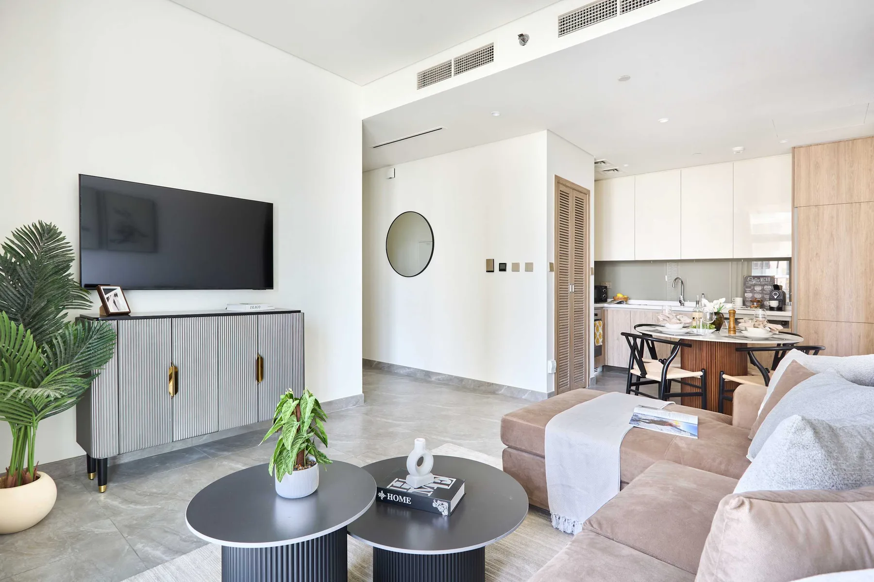 A bright living room opens into a kitchen, with seating and a television.