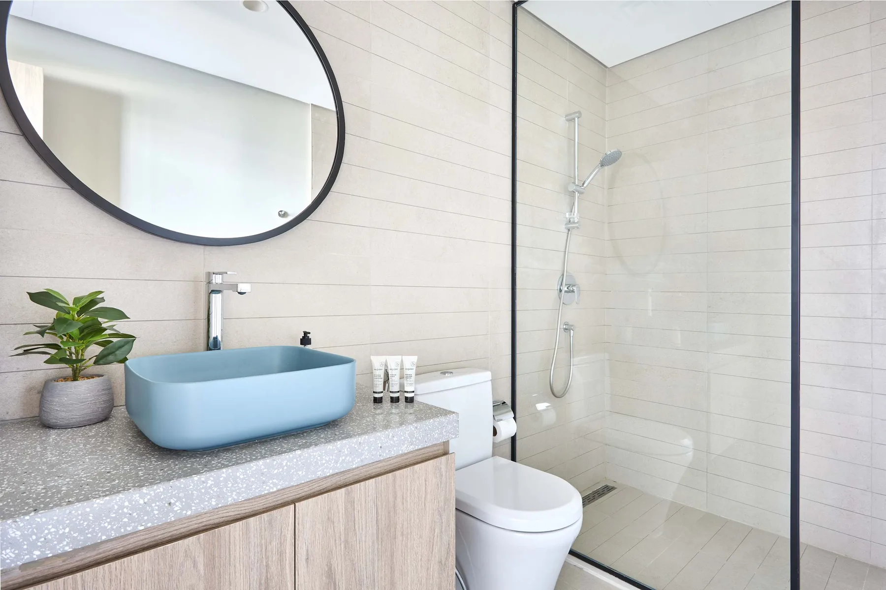 A bright bathroom with a blue vessel sink and glass shower.