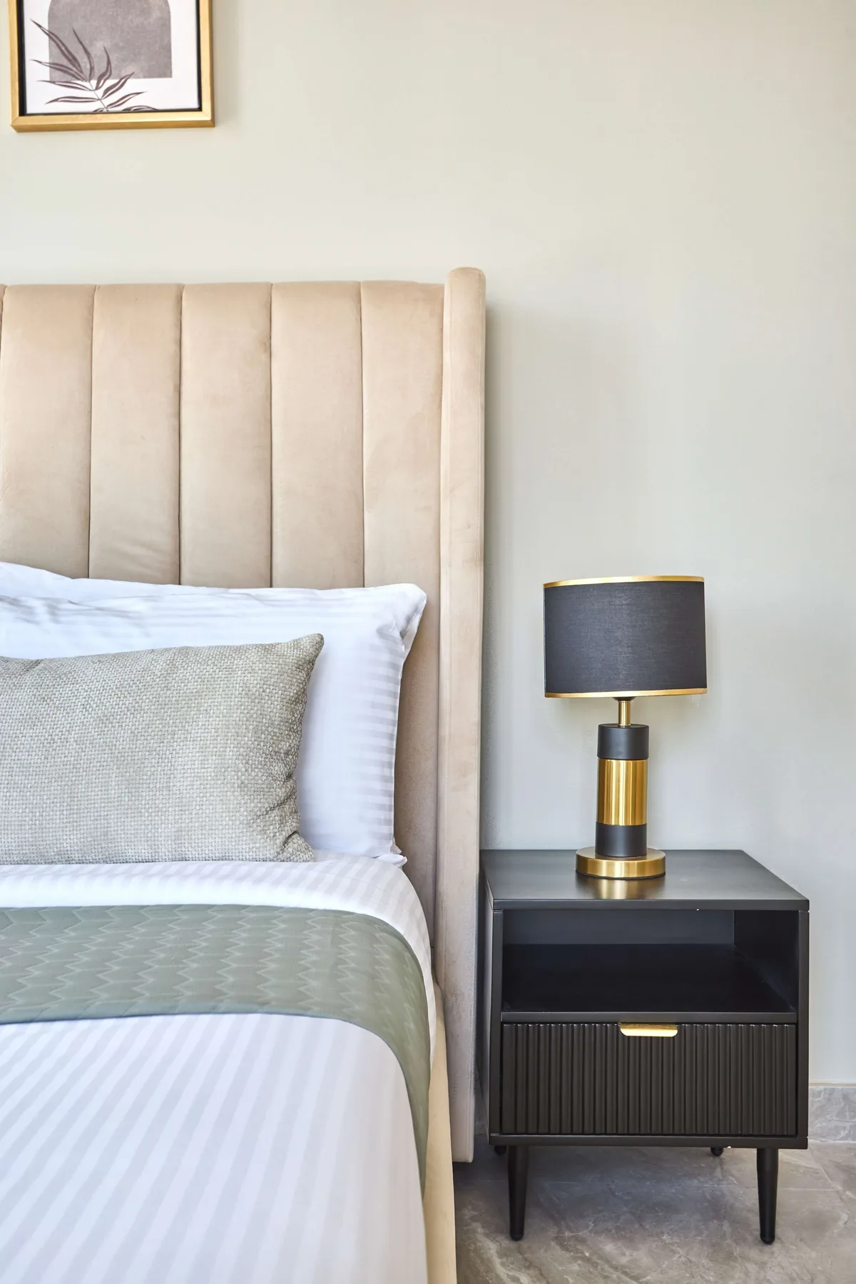 A bedroom with a neatly made bed and a bedside table with a lamp.