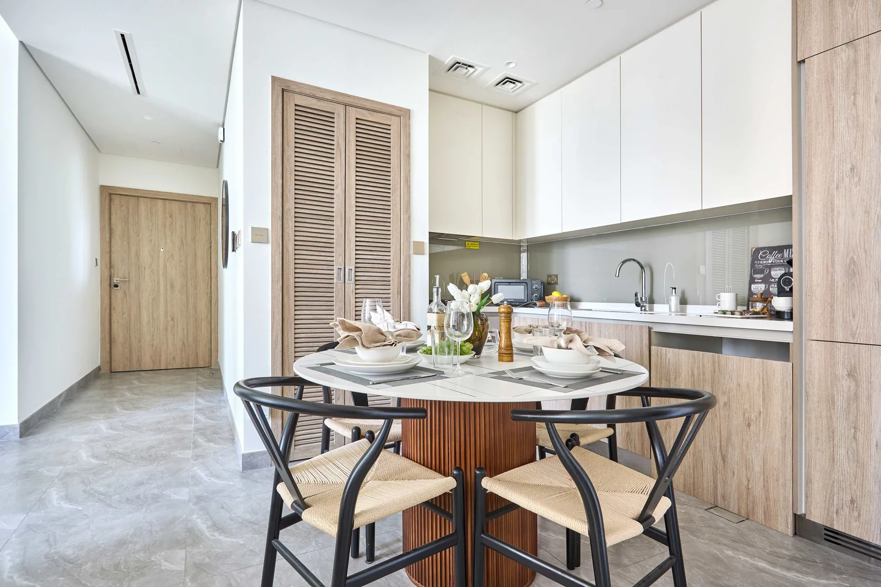 A bright dining area opens onto a compact kitchen, with a round table and chairs.