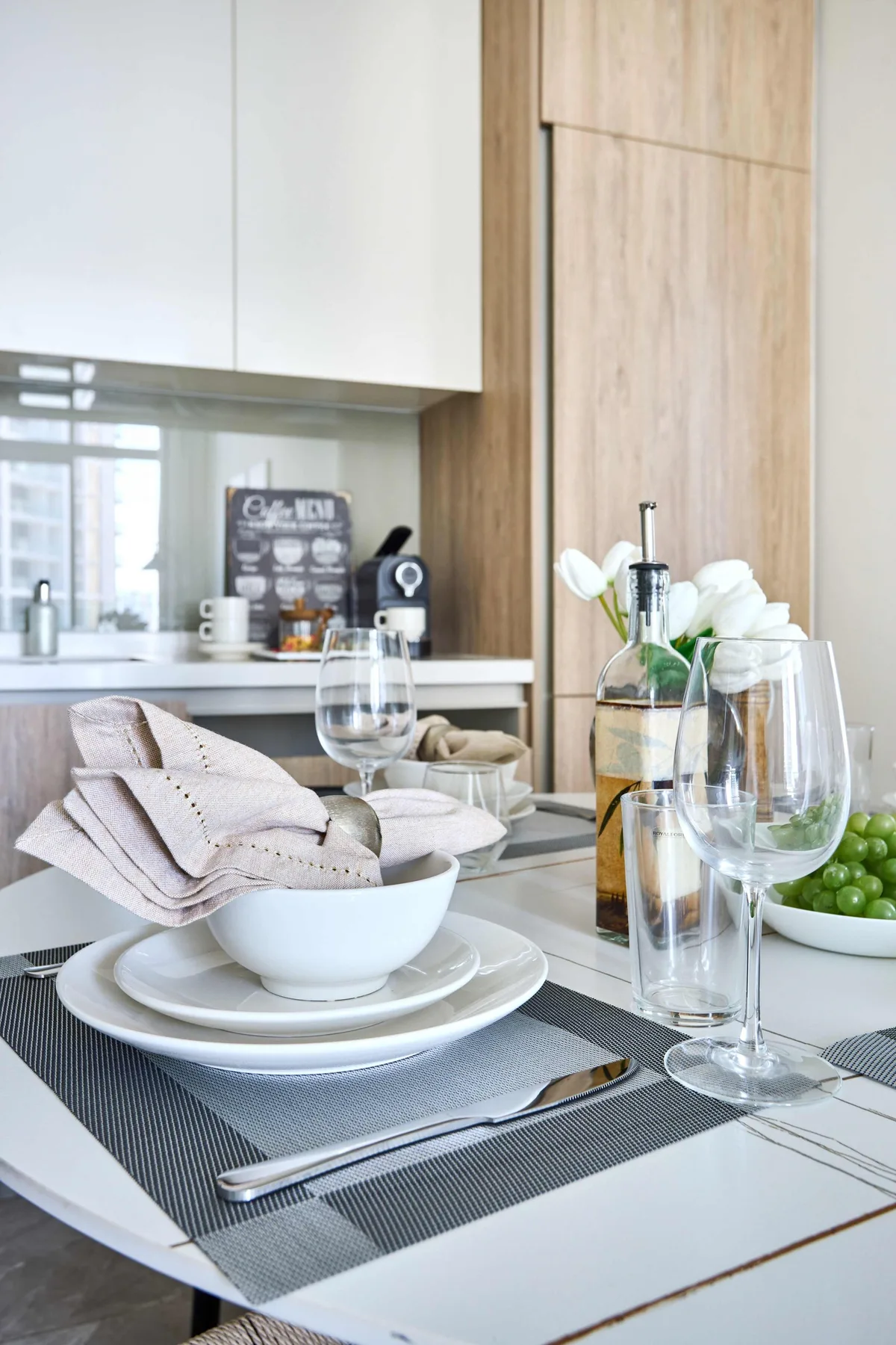A dining table is set with dishes, glasses, and flowers in a modern kitchen.
