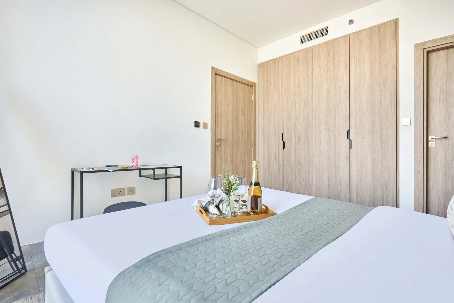 A bedroom with a bed, a console table, and light wood wardrobes.