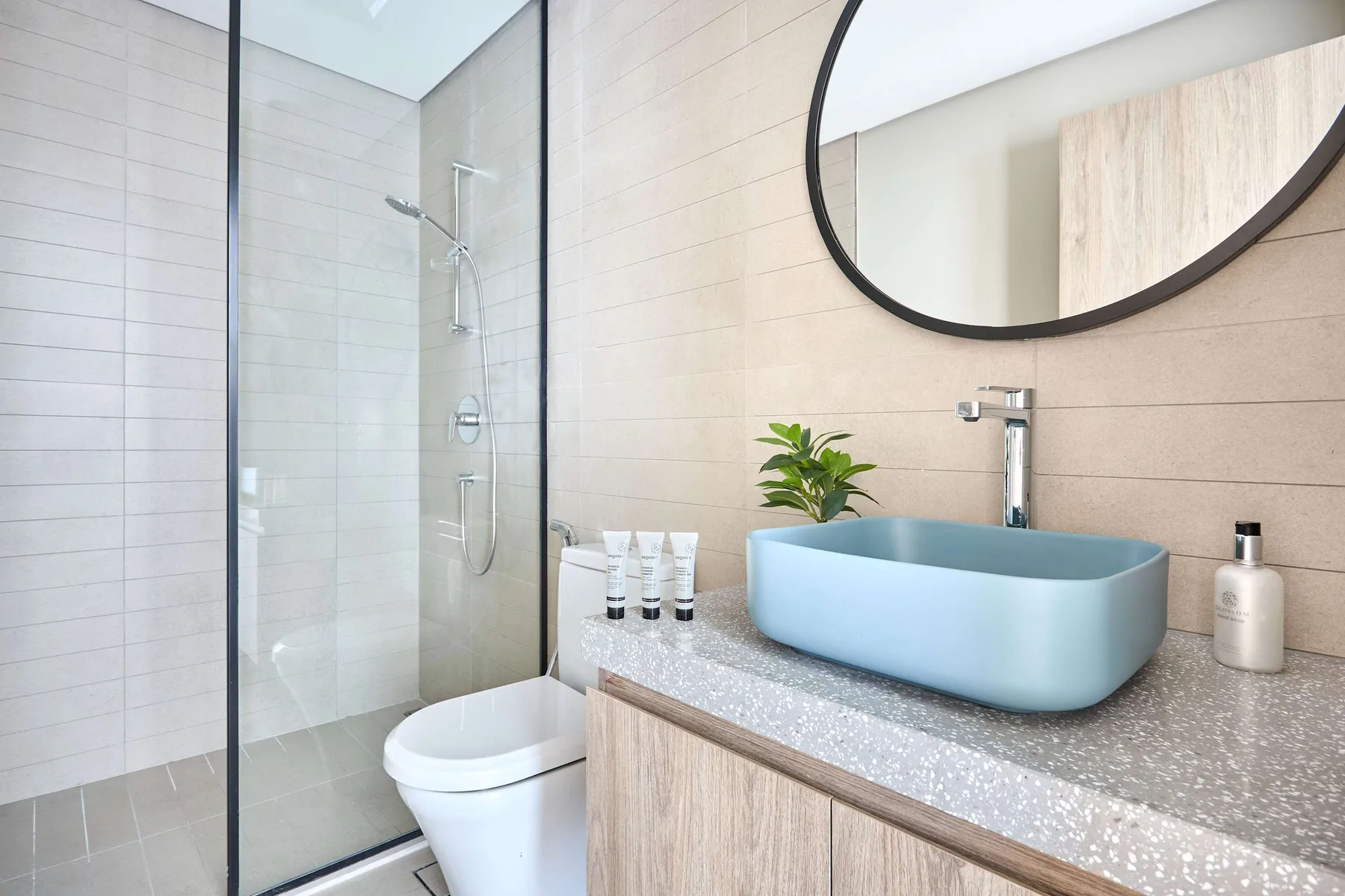 A modern bathroom with a glass shower, toilet, and pale blue vessel sink.