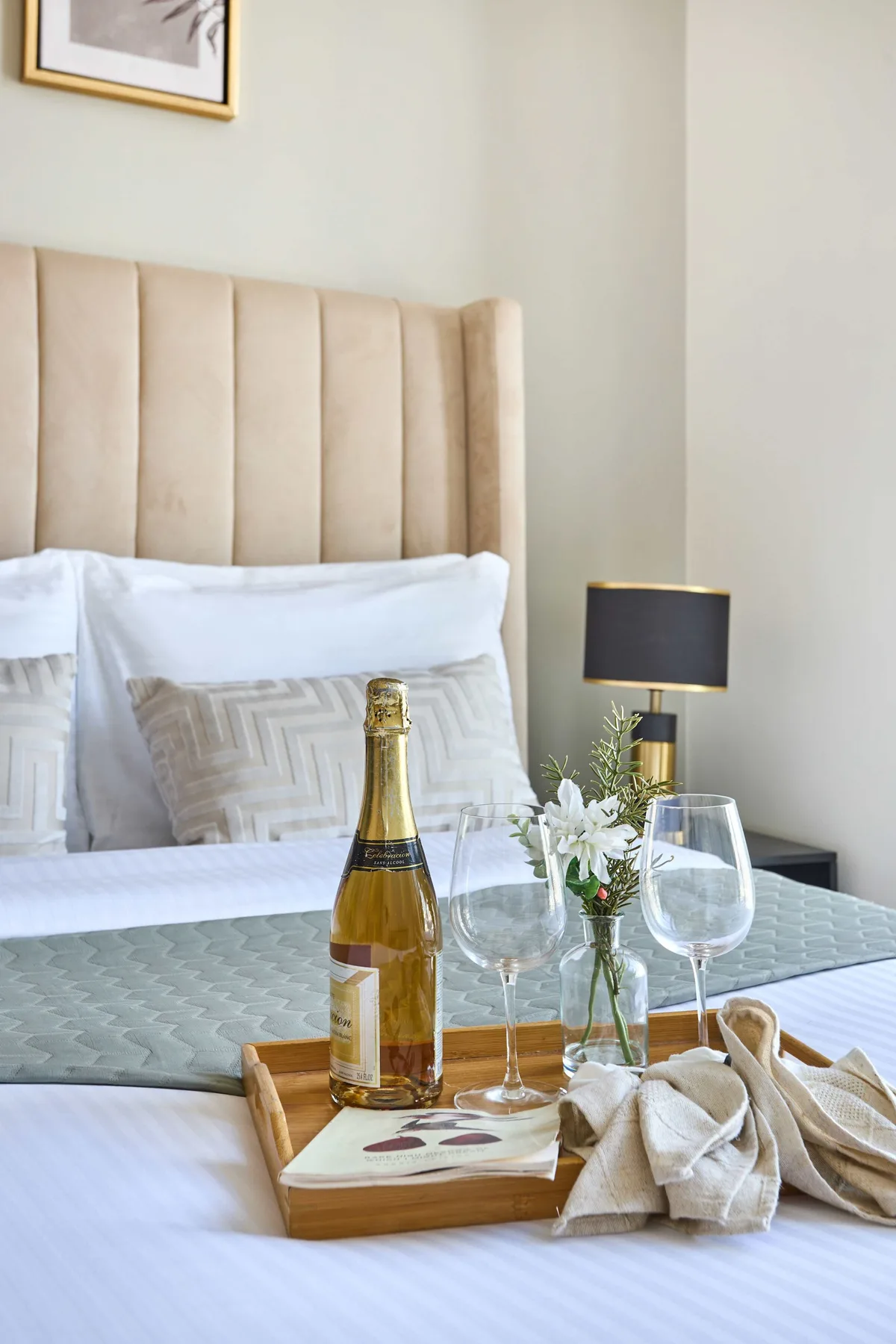 A bedroom with a neatly made bed and a tray holding drinks and flowers.