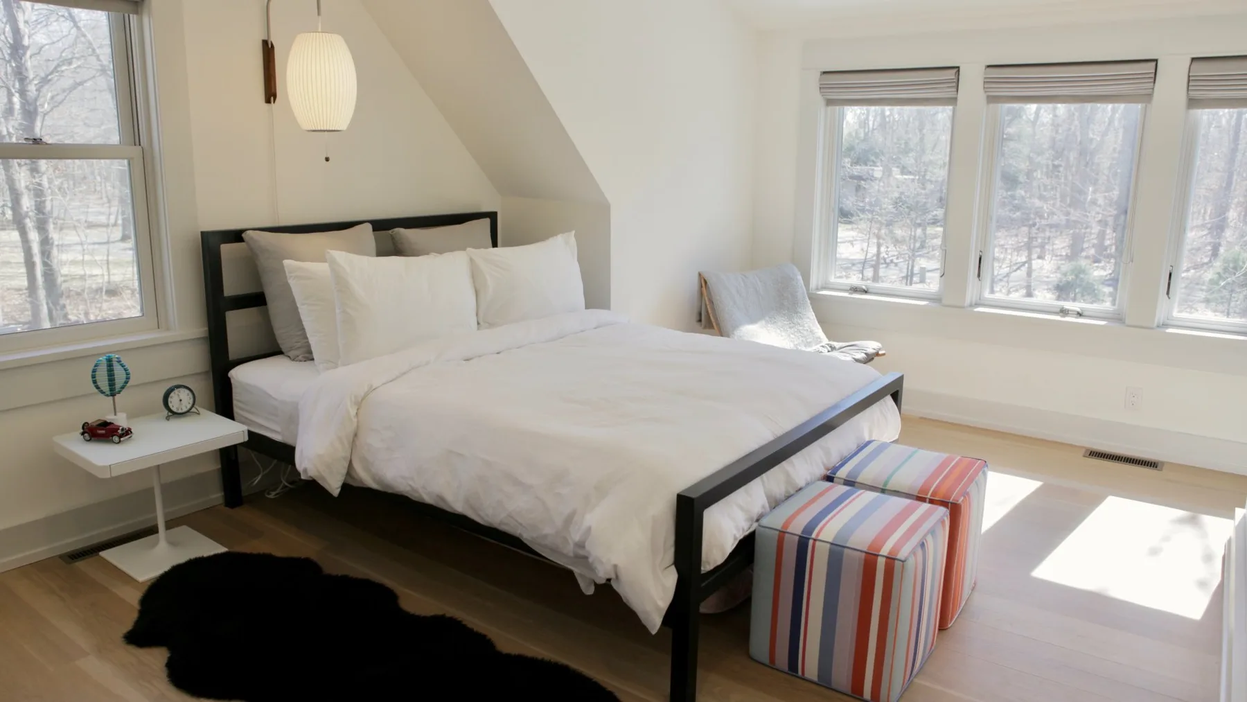 A bright bedroom with a large bed beside several windows.