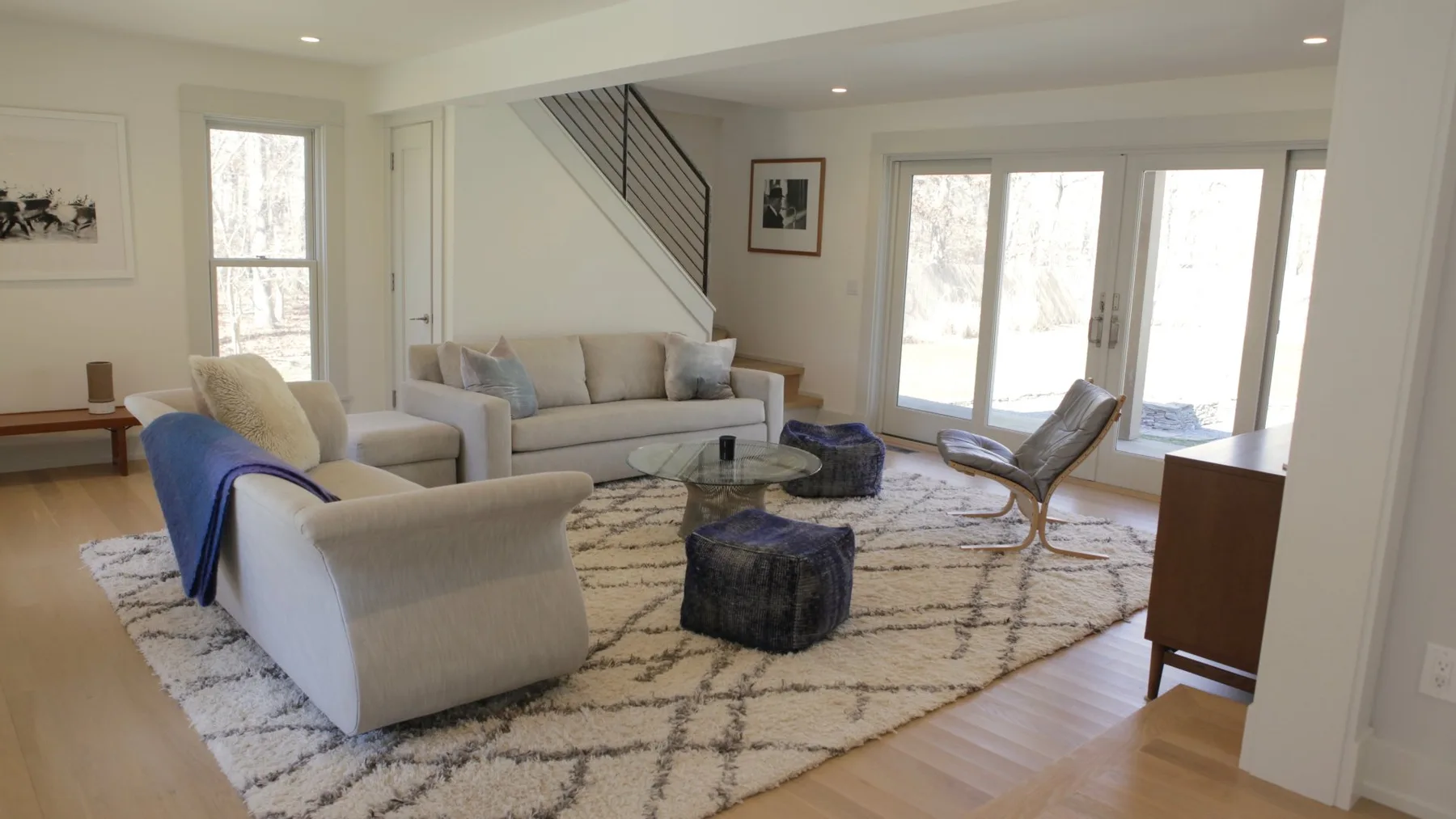 A bright living room with seating around a patterned rug and glass doors.