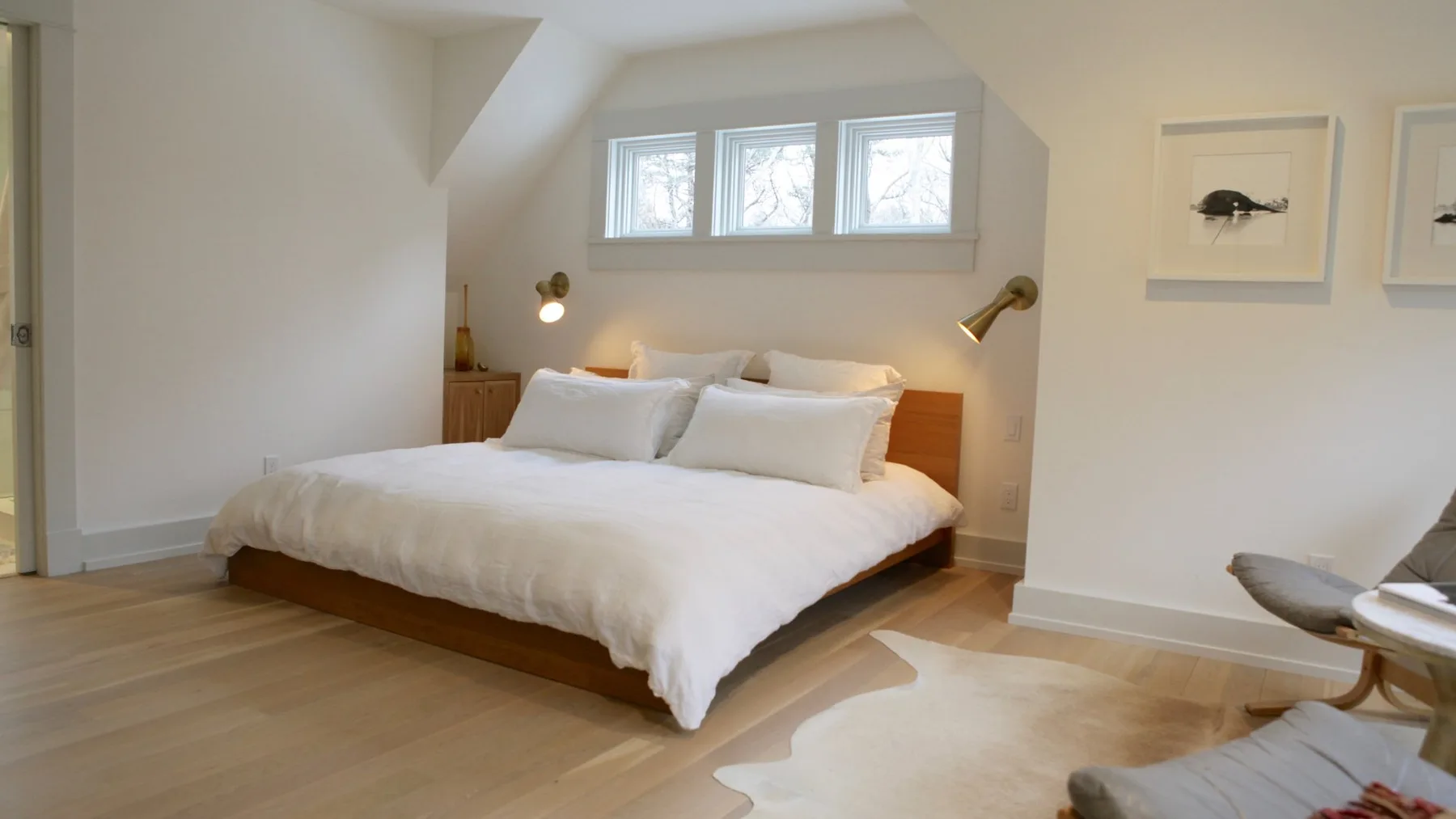 A bright bedroom with a neatly made bed beneath three windows.