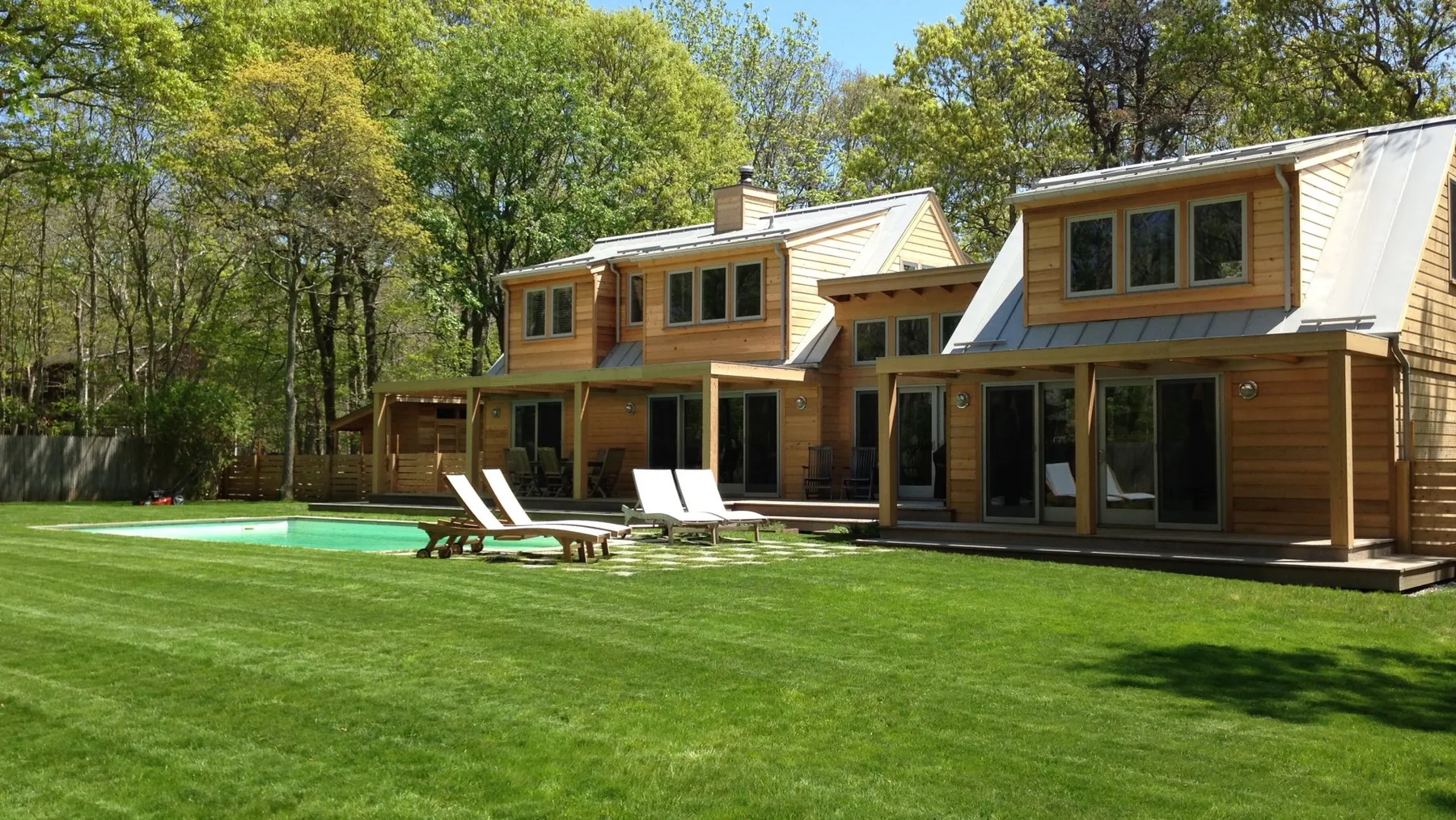 Una casa grande con revestimiento de madera junto a un césped verde y una piscina exterior.