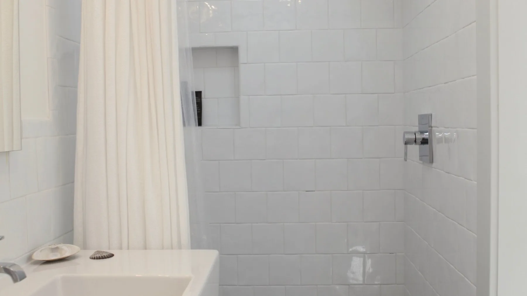 A tiled bathroom with a shower and a sink beside a curtain.