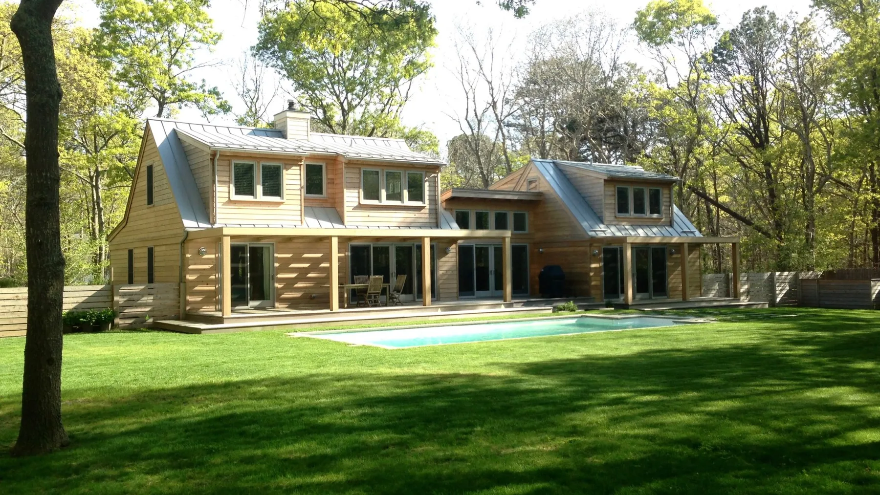 A modern house stands beside a swimming pool in a wooded yard.