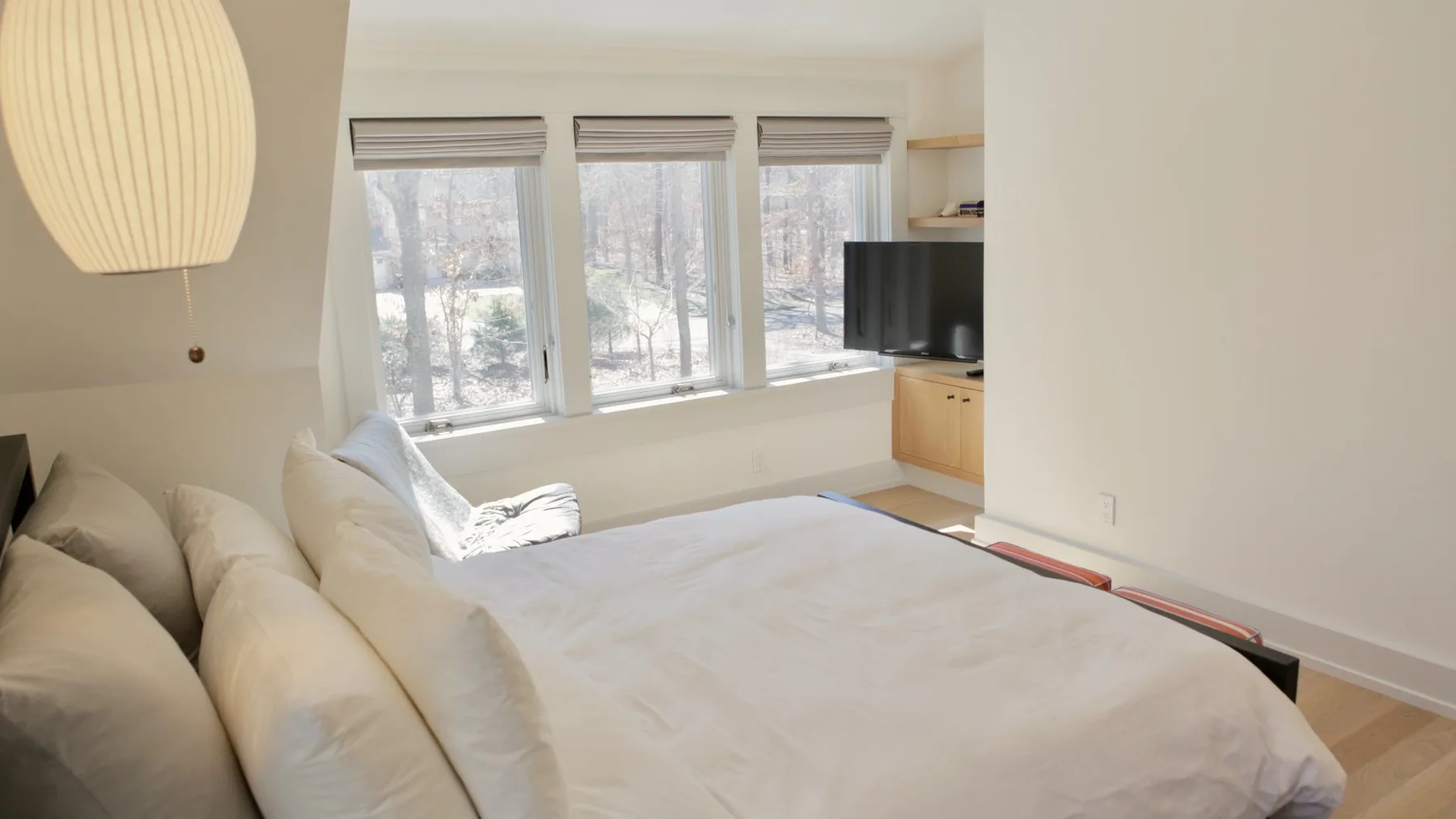 A bright bedroom with a bed beneath three large windows.