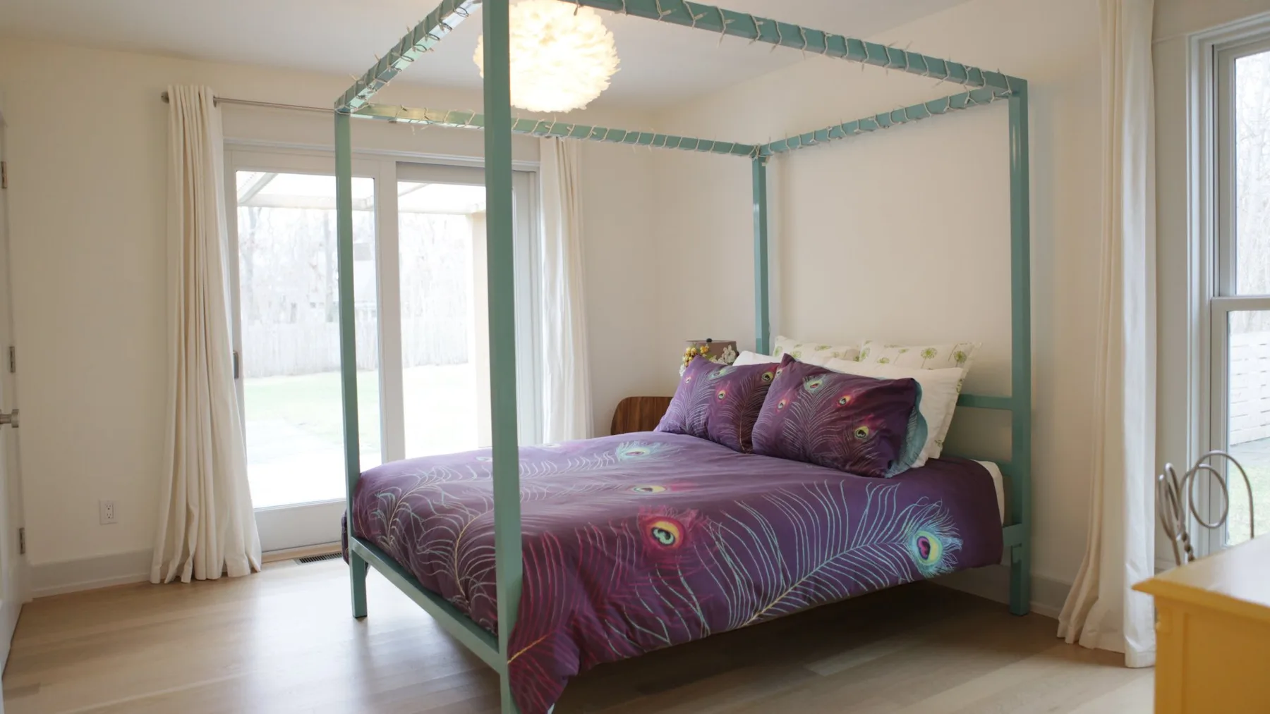 A bedroom with a purple bed beneath a canopy frame and large windows.