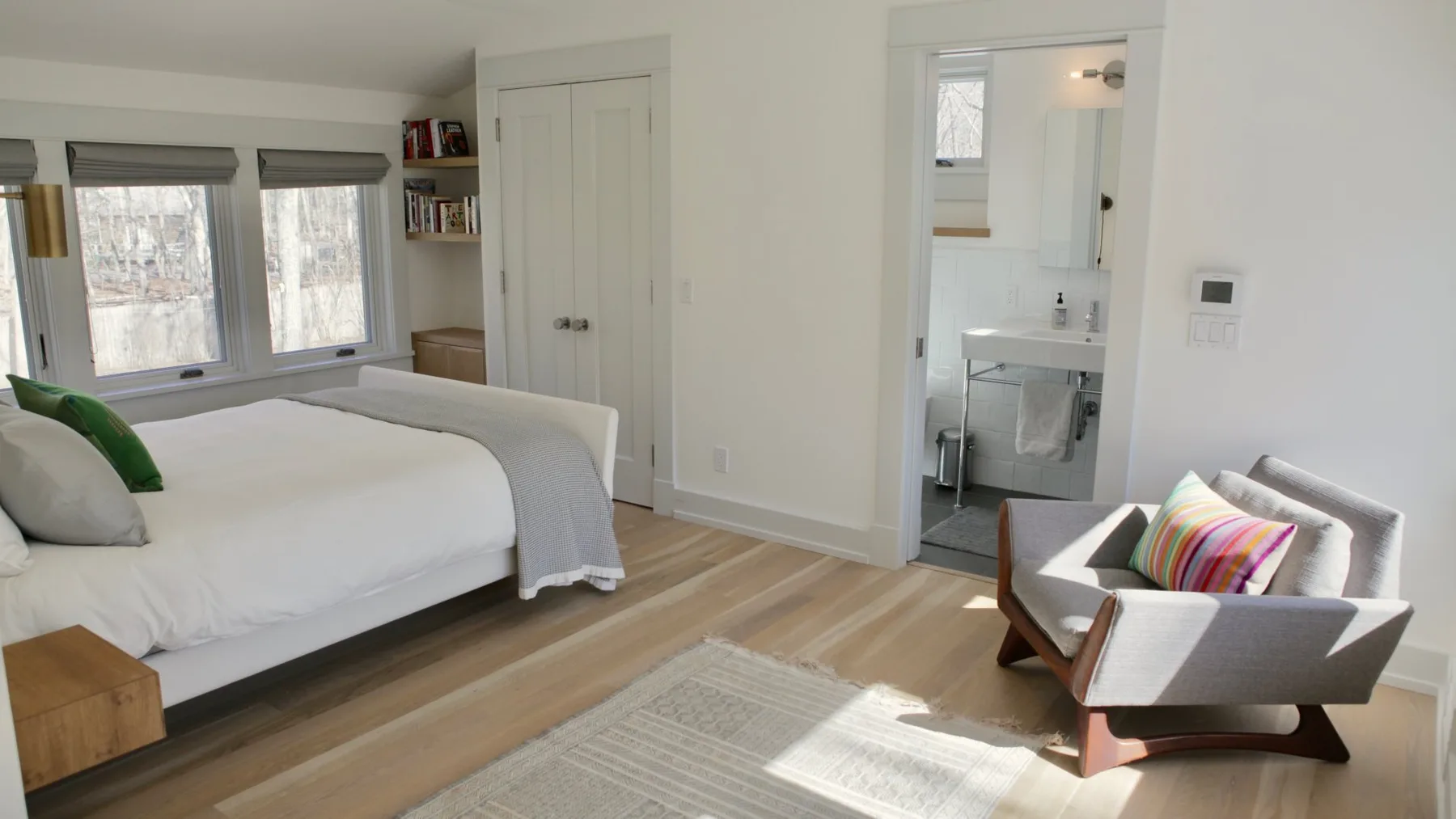 A bright bedroom with a bed and an armchair beside the bathroom doorway.