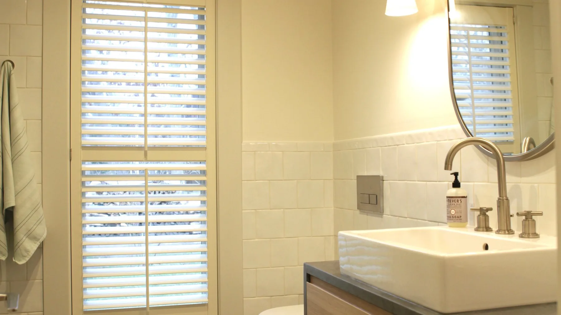 A bathroom vanity with a white basin, wall mirror, and window blinds.
