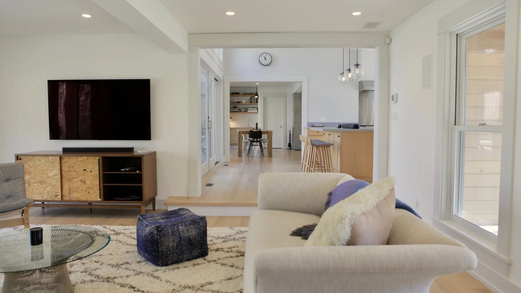 A bright living room with a television, seating, and a glass coffee table.