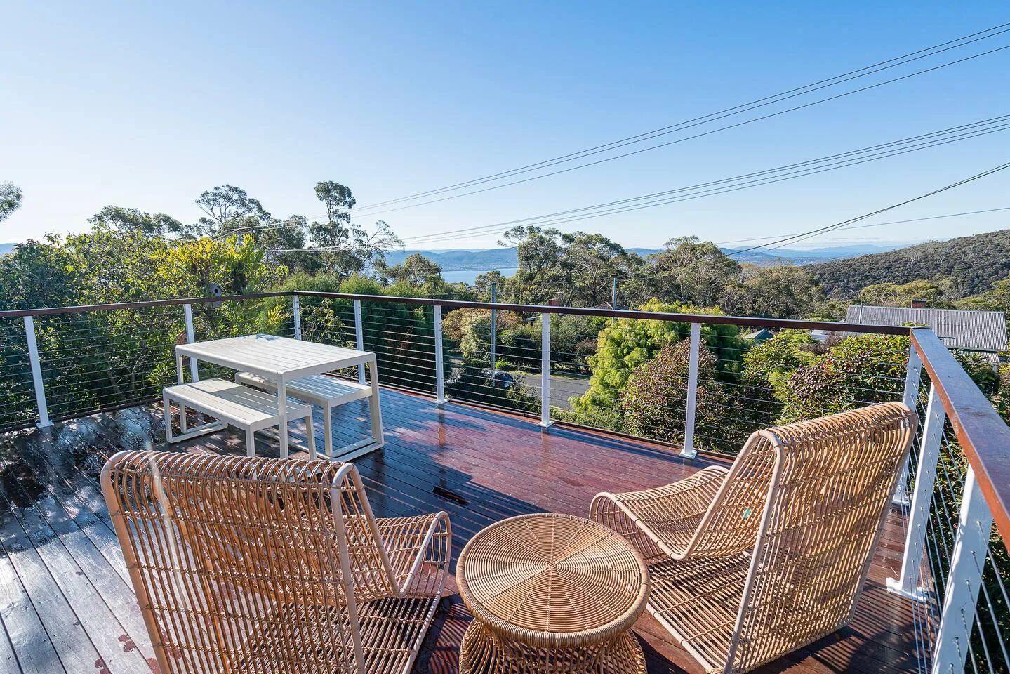 An outdoor deck has woven seating, a small table, and views over trees.