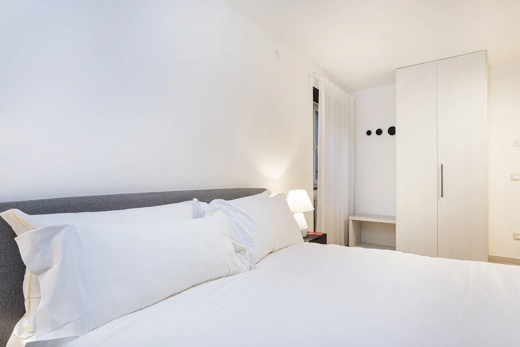 Un dormitorio luminoso con una cama bien tendida y un armario blanco alto.