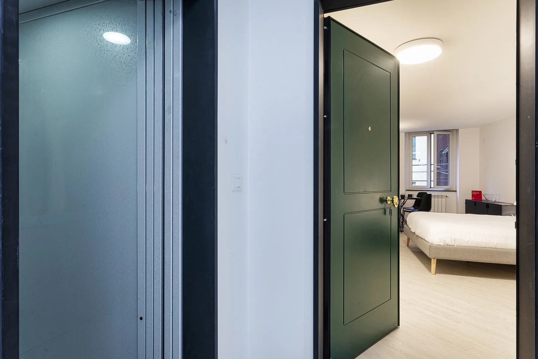 Se ve un dormitorio a través de una puerta abierta, con una cama y una ventana.