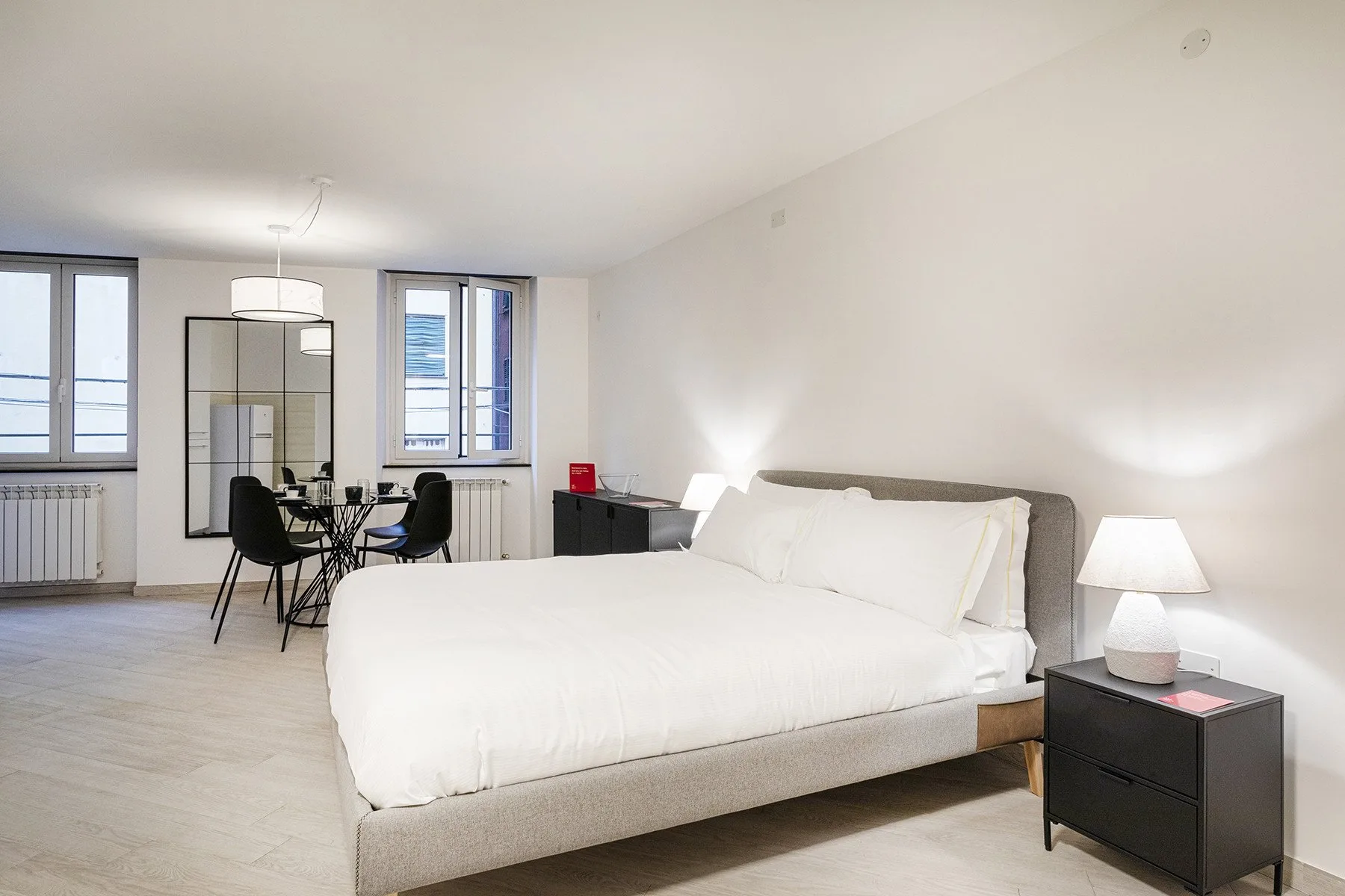 Dormitorio luminoso con una cama grande, una mesita de noche y ventanas.