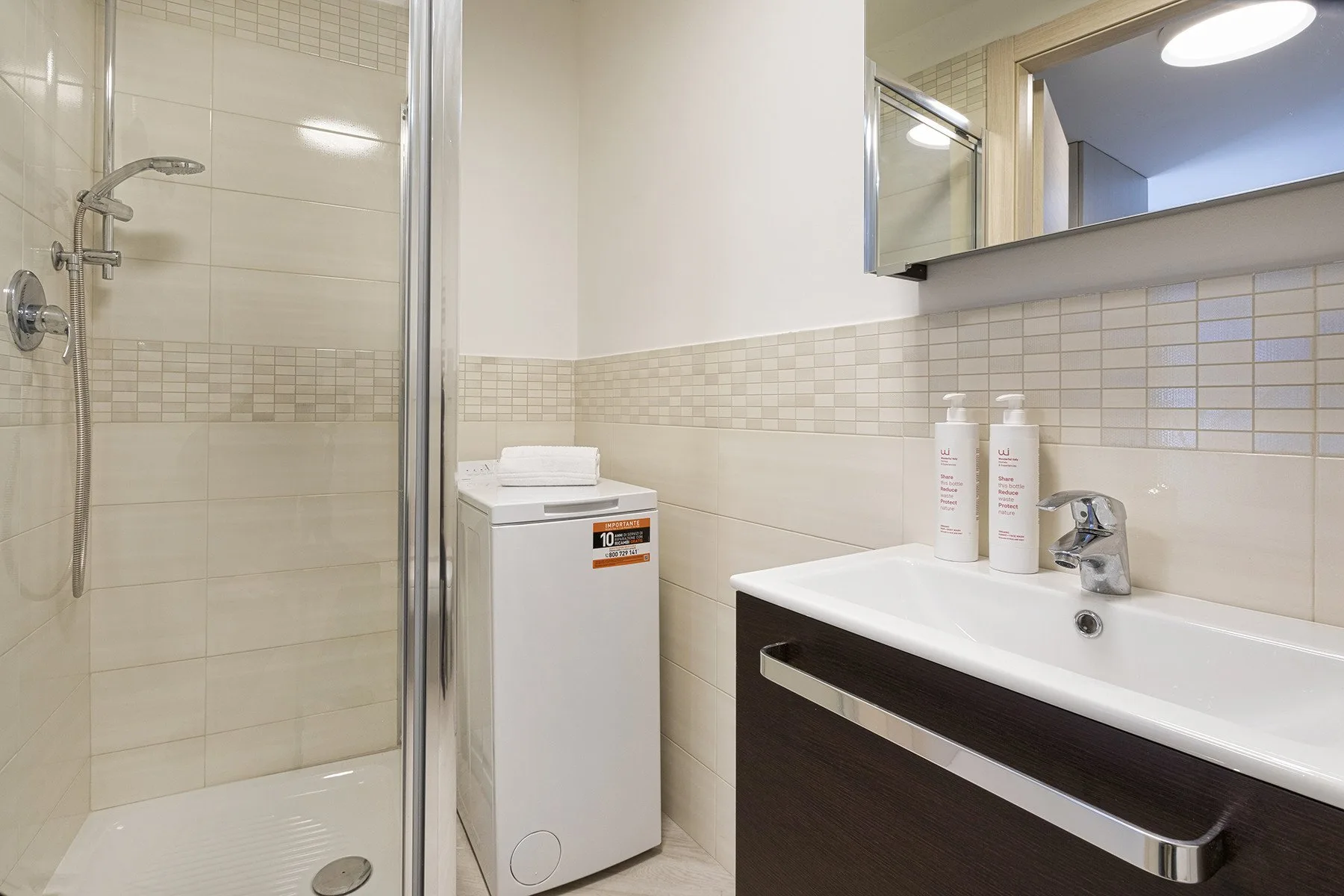 Un baño luminoso con ducha de vidrio, lavabo y lavadora.