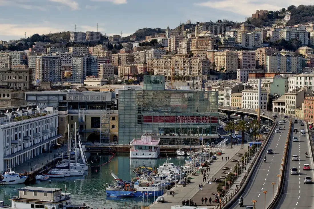 Un puerto y un paseo marítimo se encuentran bajo una colina densamente cubierta de edificios.