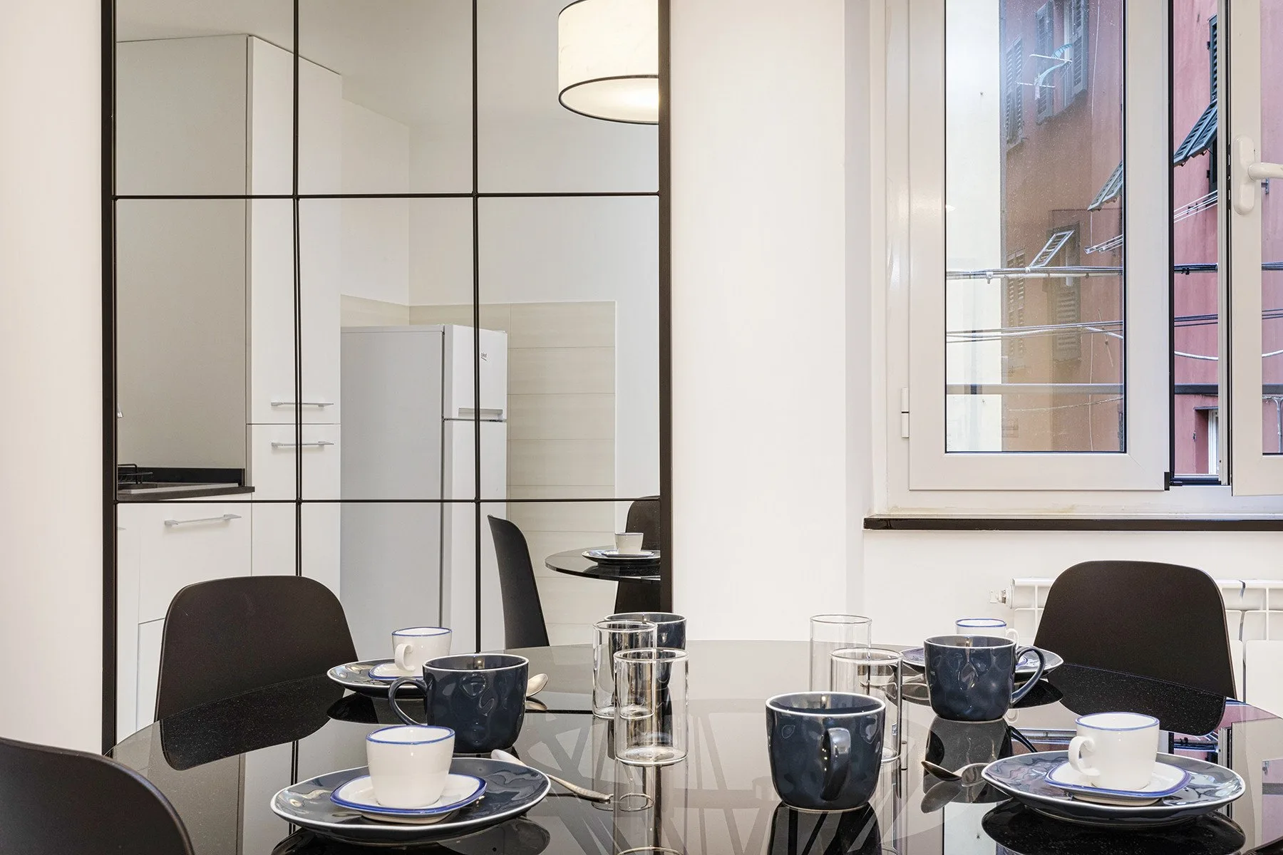 Un comedor con una mesa de cristal y asientos oscuros junto a una ventana.