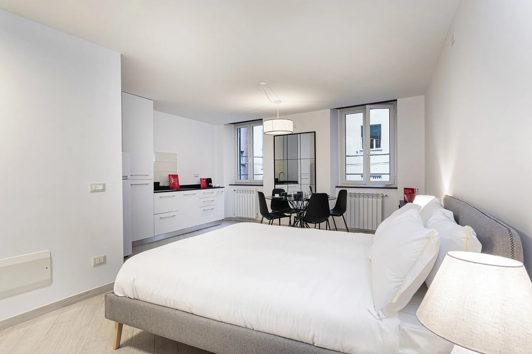 Un dormitorio luminoso con una cama grande, armarios blancos y una mesa junto a las ventanas.