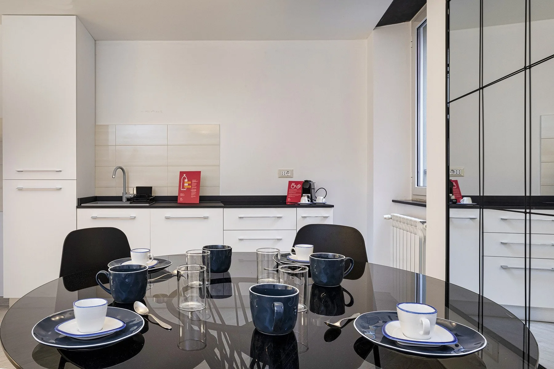 Una cocina luminosa con armarios blancos y una mesa puesta con tazas y platos.