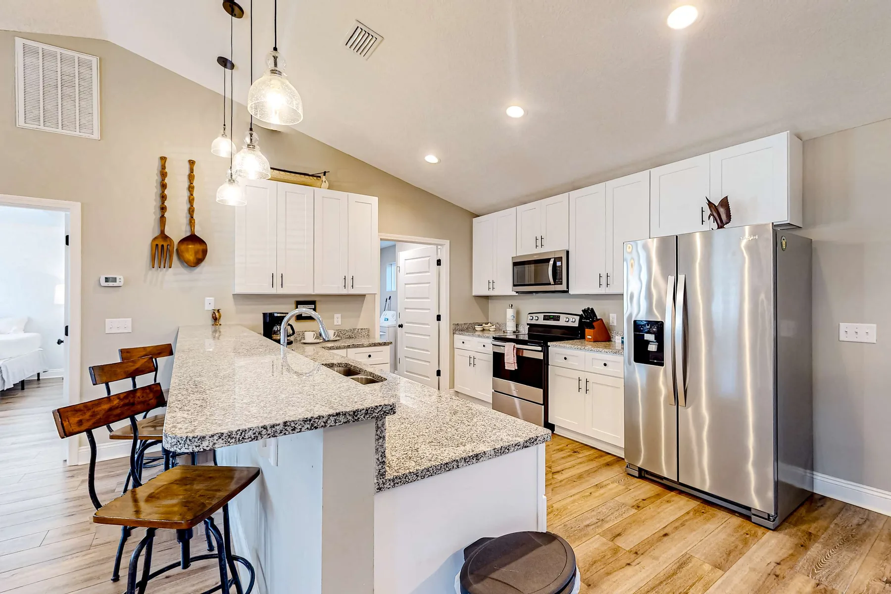A bright kitchen with a stone countertop, white cabinets, and stainless steel appliances.