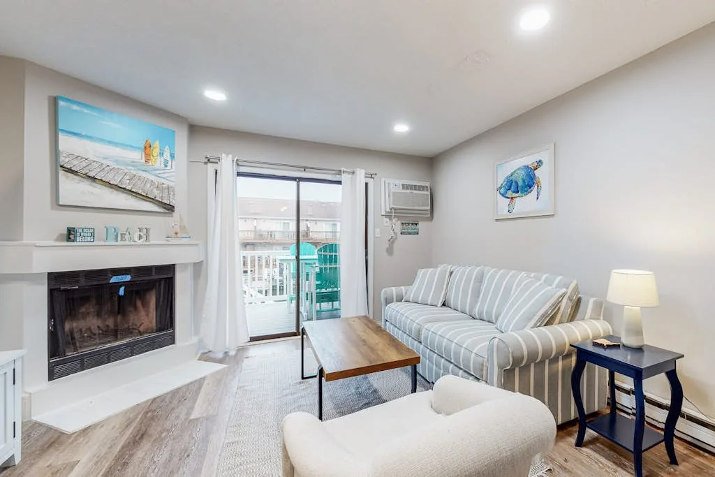 A living room with striped seating, a fireplace, and a glass door opening to a balcony.