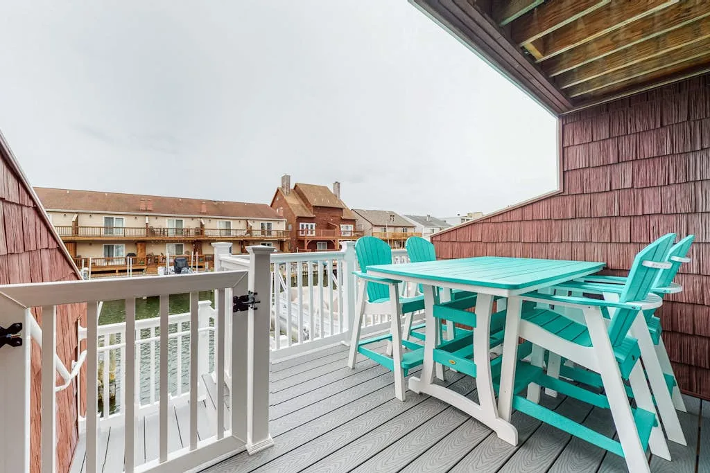 A covered outdoor deck has turquoise seating and a table overlooking nearby buildings.