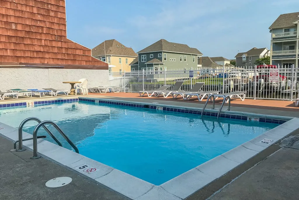 An outdoor swimming pool sits among residential buildings under a clear sky.